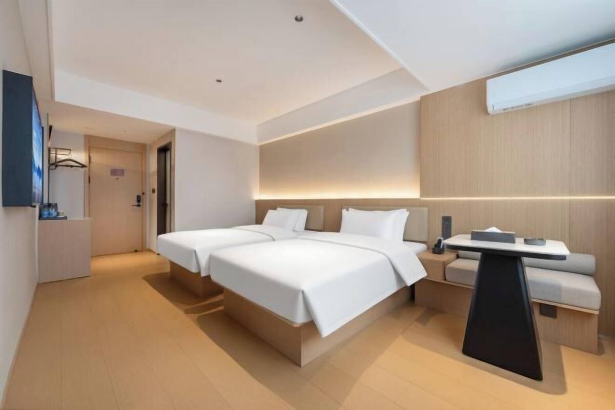 A modern hotel room with a large bed, bedside tables, a sofa, and a flat-screen TV.