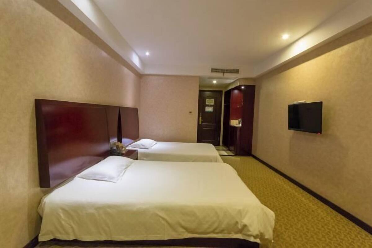 A hotel room with two beds, a television, and a hallway leading to a door.
