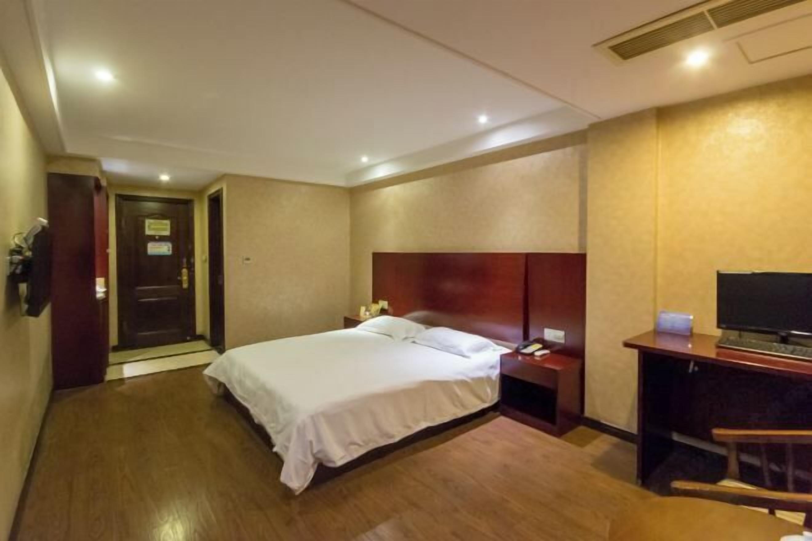 A hotel room with a bed, bedside table, desk with a chair, and a television.