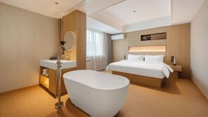 A modern hotel room with a large bathtub, a bed, a vanity with a mirror, and a bedside table. - Winchi Joyu Hostel (Wenzhou)