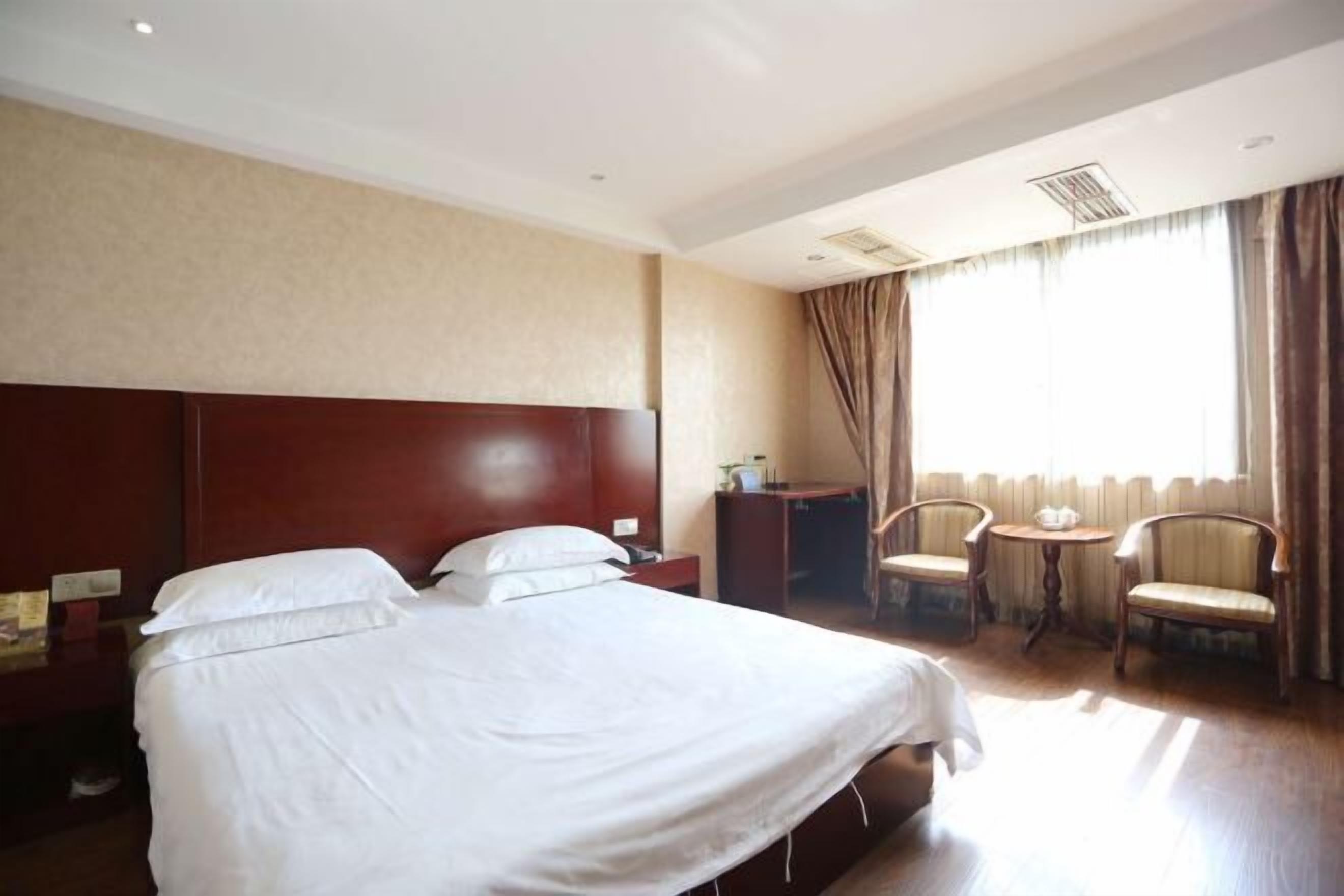 A hotel room with a large bed, a desk, two chairs, and a window with curtains.