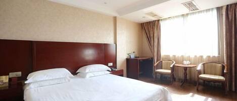 A hotel room with a large bed, a desk, two chairs, and a window with curtains.