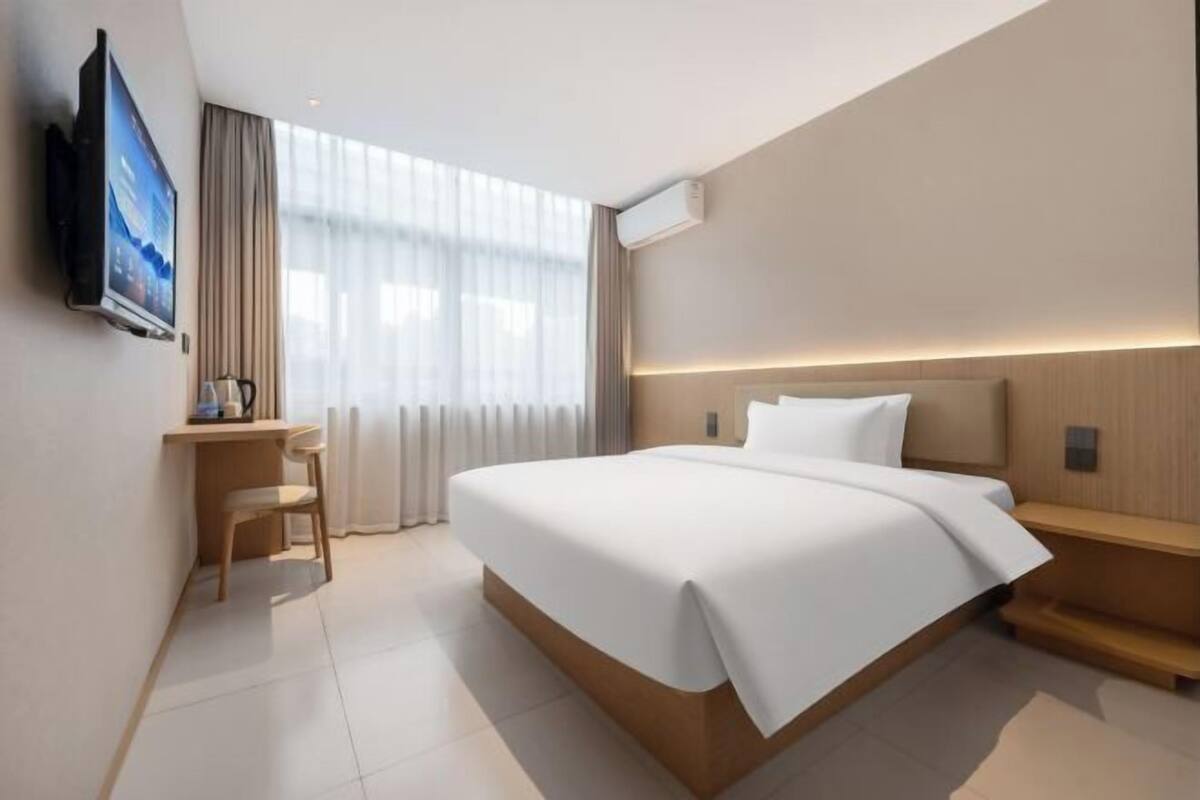 A modern hotel room with a large bed, a desk, and a TV mounted on the wall.