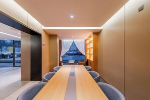 A hotel room with a long wooden table, comfortable seating, a view through a window with sheer curtains, and a bookshelf. - Homeinn Hotel ( Ningbo K11 Shopping Center, Jiangxia Bridge Metro Station Branch） (Ningbo)