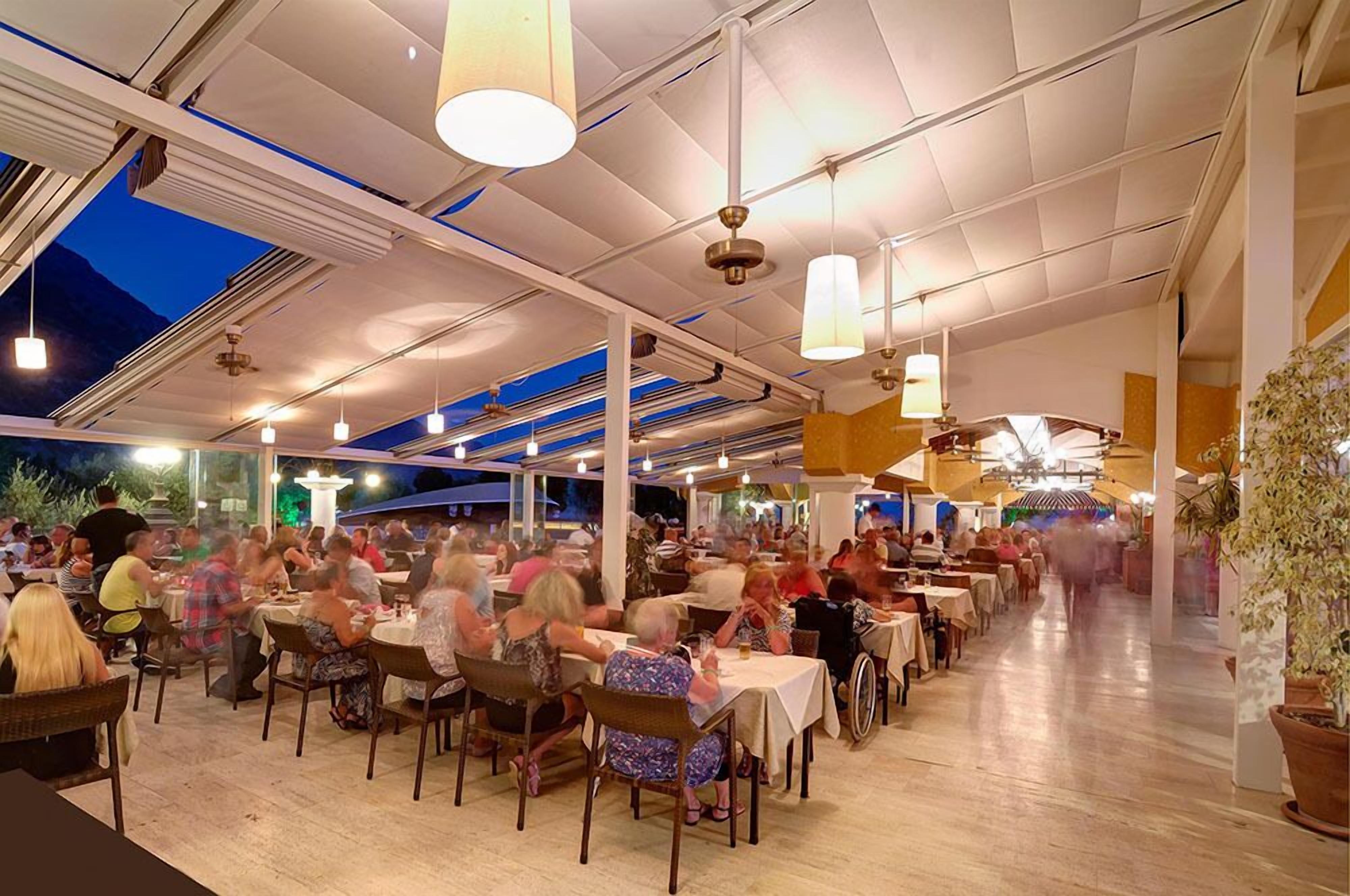 An outdoor dining area with tables and chairs, covered by a roof with hanging lights.