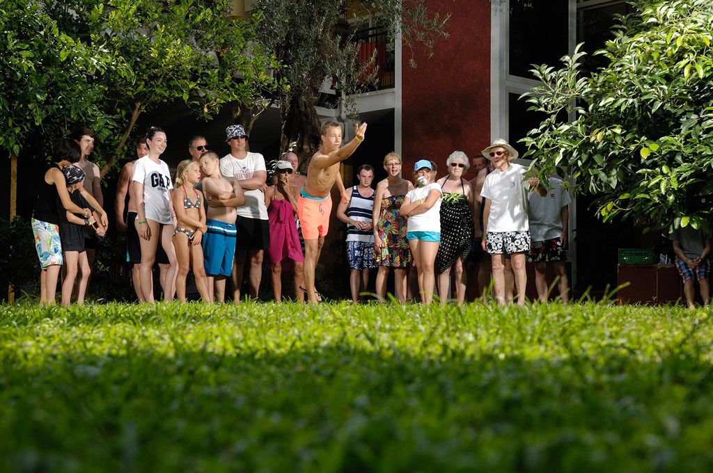 Un grupo de personas de pie al aire libre en una zona verde con árboles y un edificio al fondo.