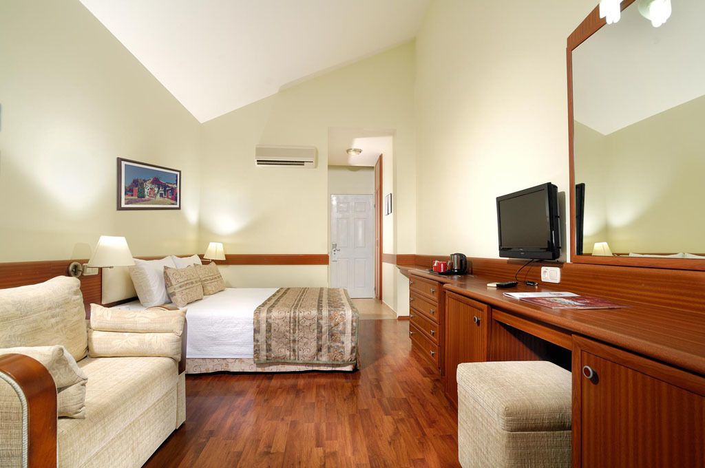 A hotel room with a bed, two armchairs, a wooden dresser, a television, and a large mirror.