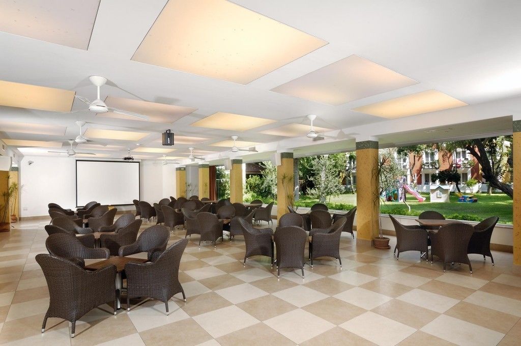 A spacious outdoor seating area with multiple tables and chairs, a ceiling with recessed lighting, and a view of a playground in the background.