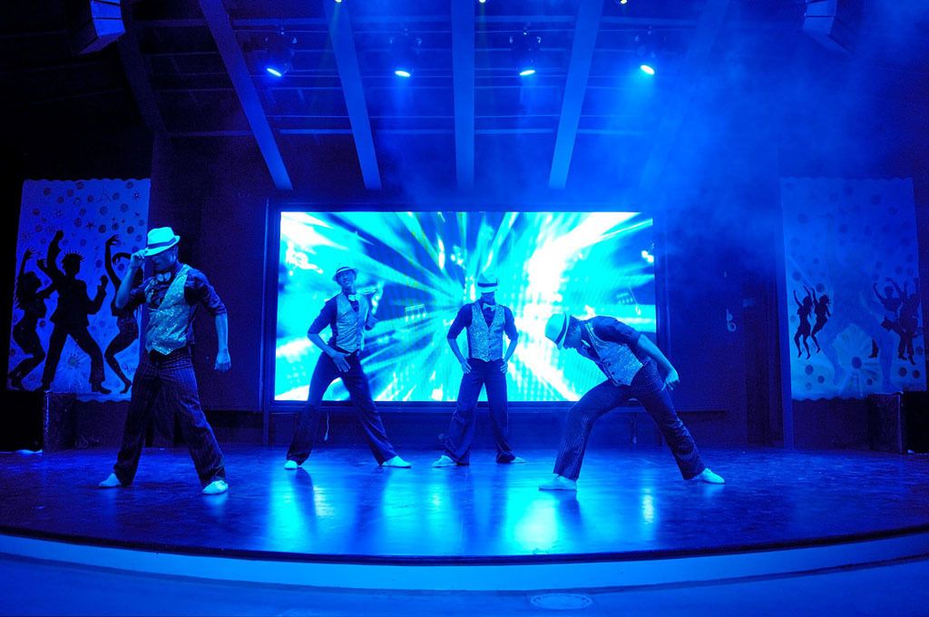 Une scène où des danseurs se produisent devant un grand écran qui diffuse des images abstraites.