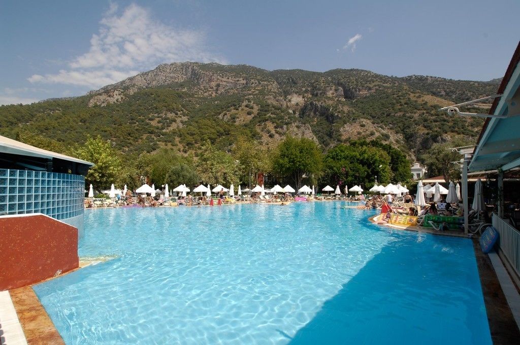 A swimming pool with lounge chairs and umbrellas, surrounded by mountains.