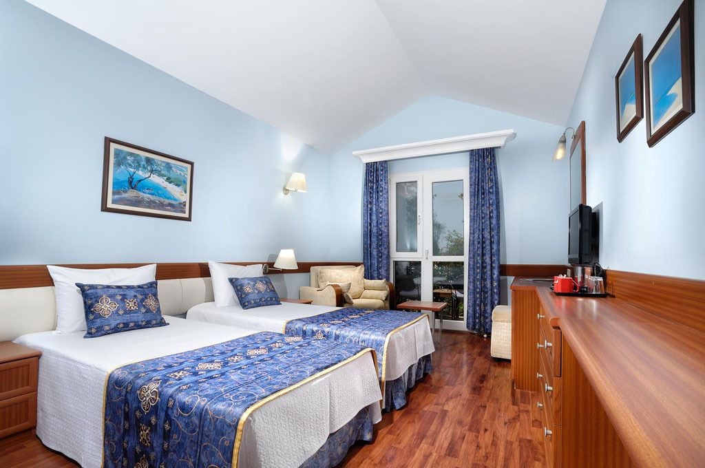 A hotel room with two beds, a TV, a desk, and a window with curtains.