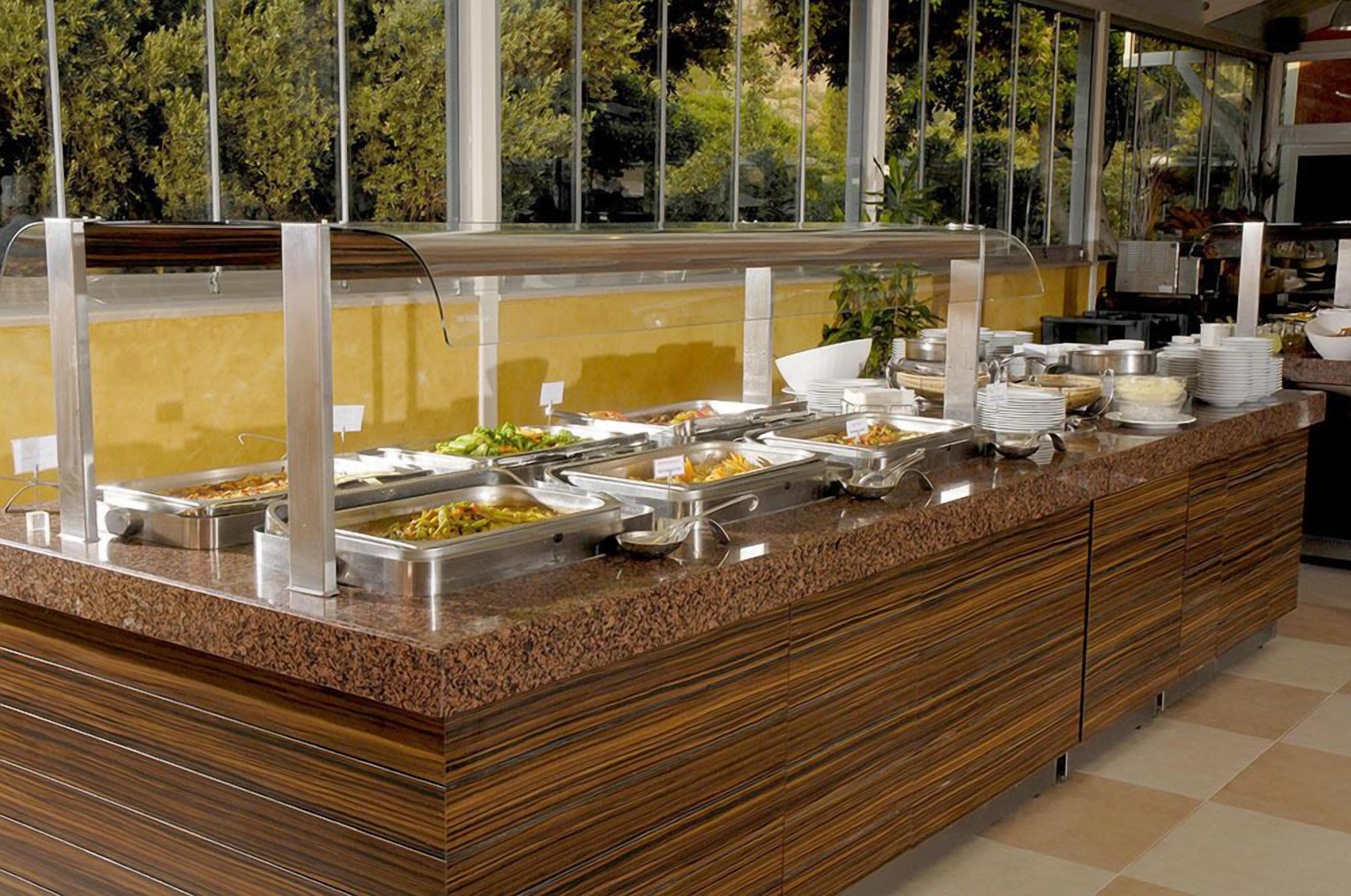 A buffet with various food items and a view of greenery outside.