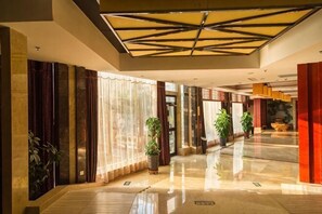 A spacious lobby with a high ceiling, large windows, and potted plants. - Huadong Hotel (Qitaihe (Xinjiang))