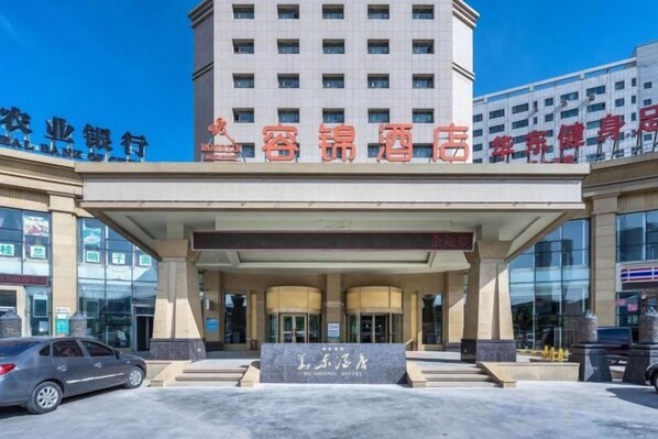 A hotel entrance with a large sign, a car parked in front, and a building in the background.
