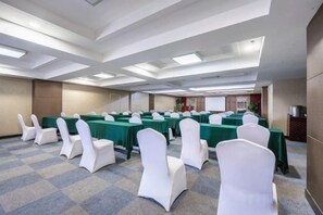 A conference room with rows of tables and chairs, a projector screen, and a kitchen area. - Huadong Hotel (Qitaihe (Xinjiang))