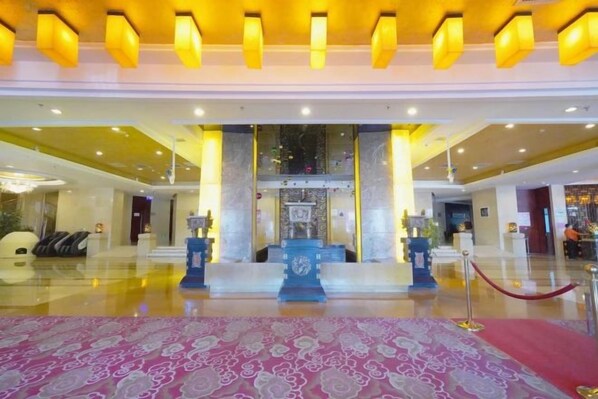 Un hall de hotel con mostrador de recepción, alfombra roja y una columna decorativa grande.