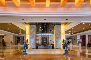 A spacious lobby with a central reception desk, marble columns, and a polished floor.