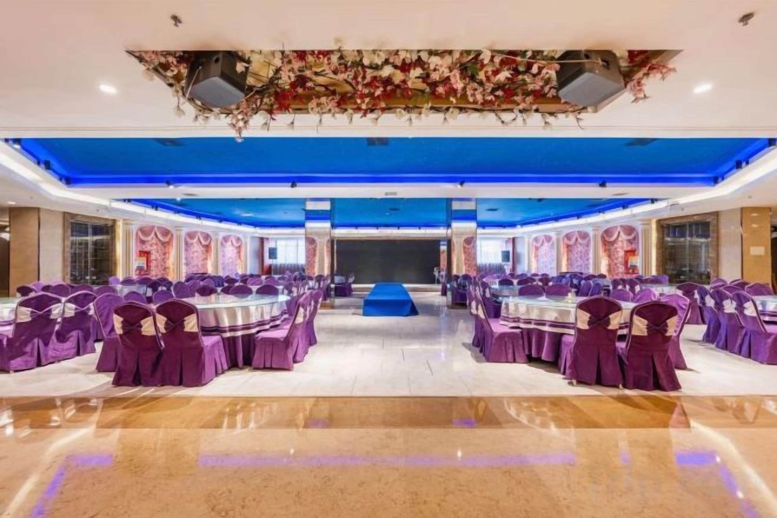 A banquet hall with round tables and purple chairs, a stage, and a blue ceiling.