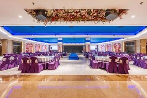 A banquet hall with round tables and purple chairs, a stage, and a blue ceiling. - Huadong Hotel (Qitaihe (Xinjiang))