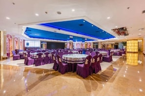 A banquet hall with round tables and purple chairs, a polished floor, and a blue ceiling.