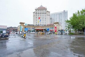A multi-story hotel with a central entrance, surrounded by a wet street and parked vehicles.