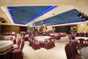 A banquet hall with round tables and chairs, a starry ceiling design, and a reflective wall.