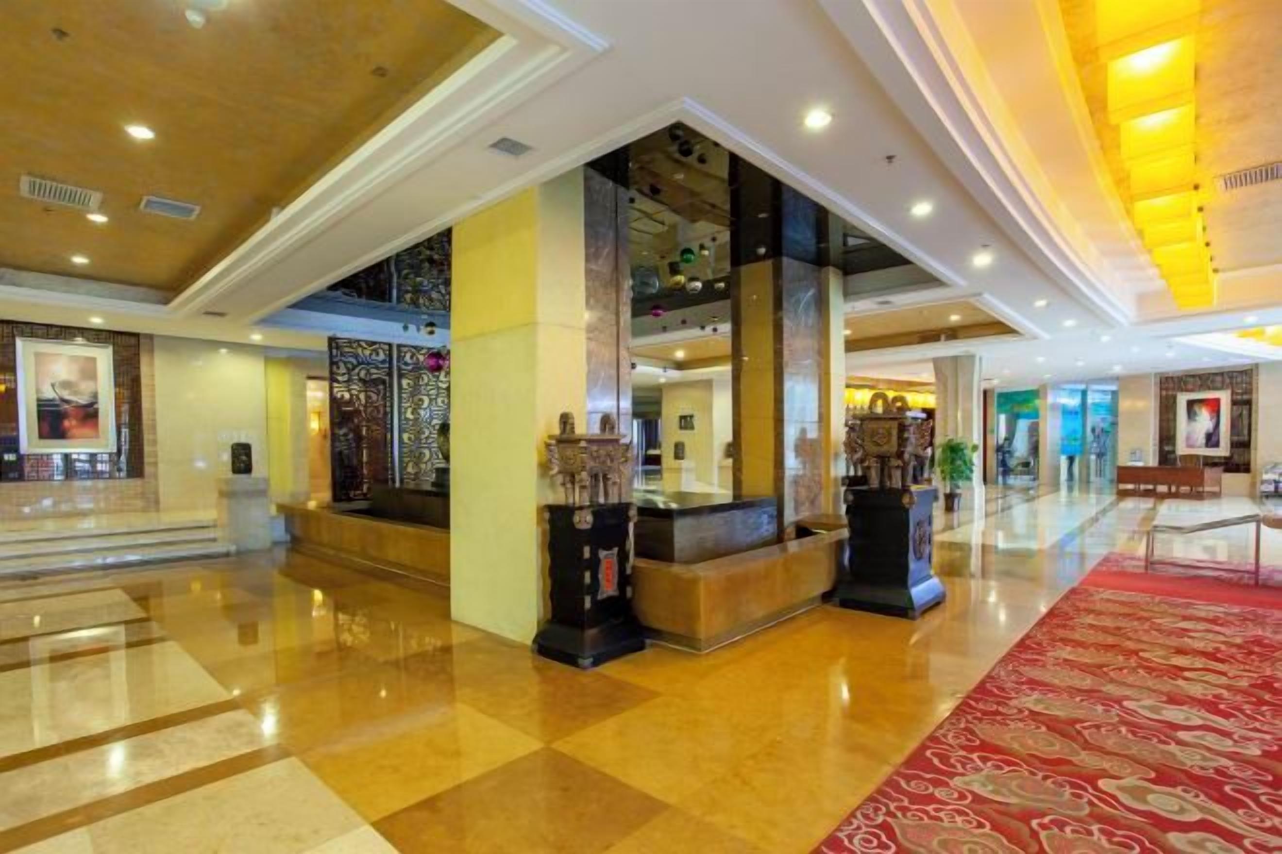 A hotel lobby with a reception desk, a red carpet, and a staircase leading to an upper level.