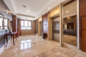 A spacious lobby with a marble floor, a reception desk, a large sliding glass door, and a modern elevator. - Huadong Hotel (Qitaihe (Xinjiang))