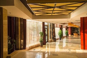 A spacious hotel lobby with a high ceiling, large windows, and potted plants. - Huadong Hotel (Qitaihe (Xinjiang))