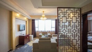 A hotel room with a TV, a sofa, a coffee table, and a decorative partition. - Huadong Hotel (Qitaihe (Xinjiang))