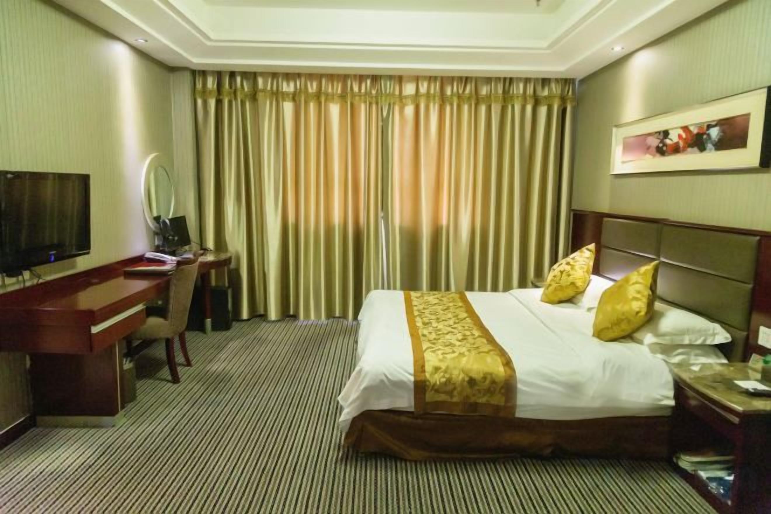 A hotel room with a bed, a desk, a television, and curtains.