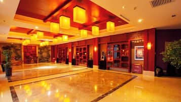 A spacious lobby with a polished marble floor, red walls, and multiple hanging light fixtures.