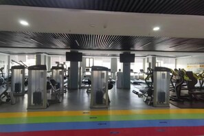 A gym with exercise machines, a central pillar, and a colorful floor design. - Huadong Hotel (Qitaihe (Xinjiang))