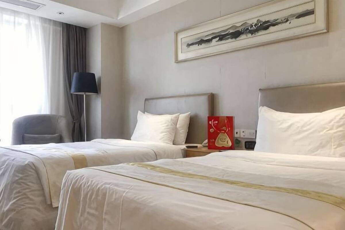 Une chambre d’hôtel avec deux lits, une table de chevet, une lampe, une chaise et un tableau au mur.