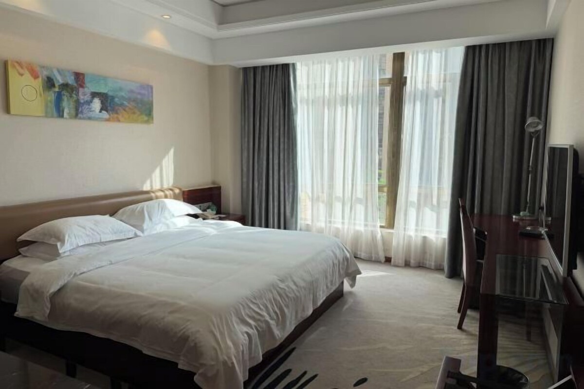 A hotel room with a large bed, a desk, and a chair.