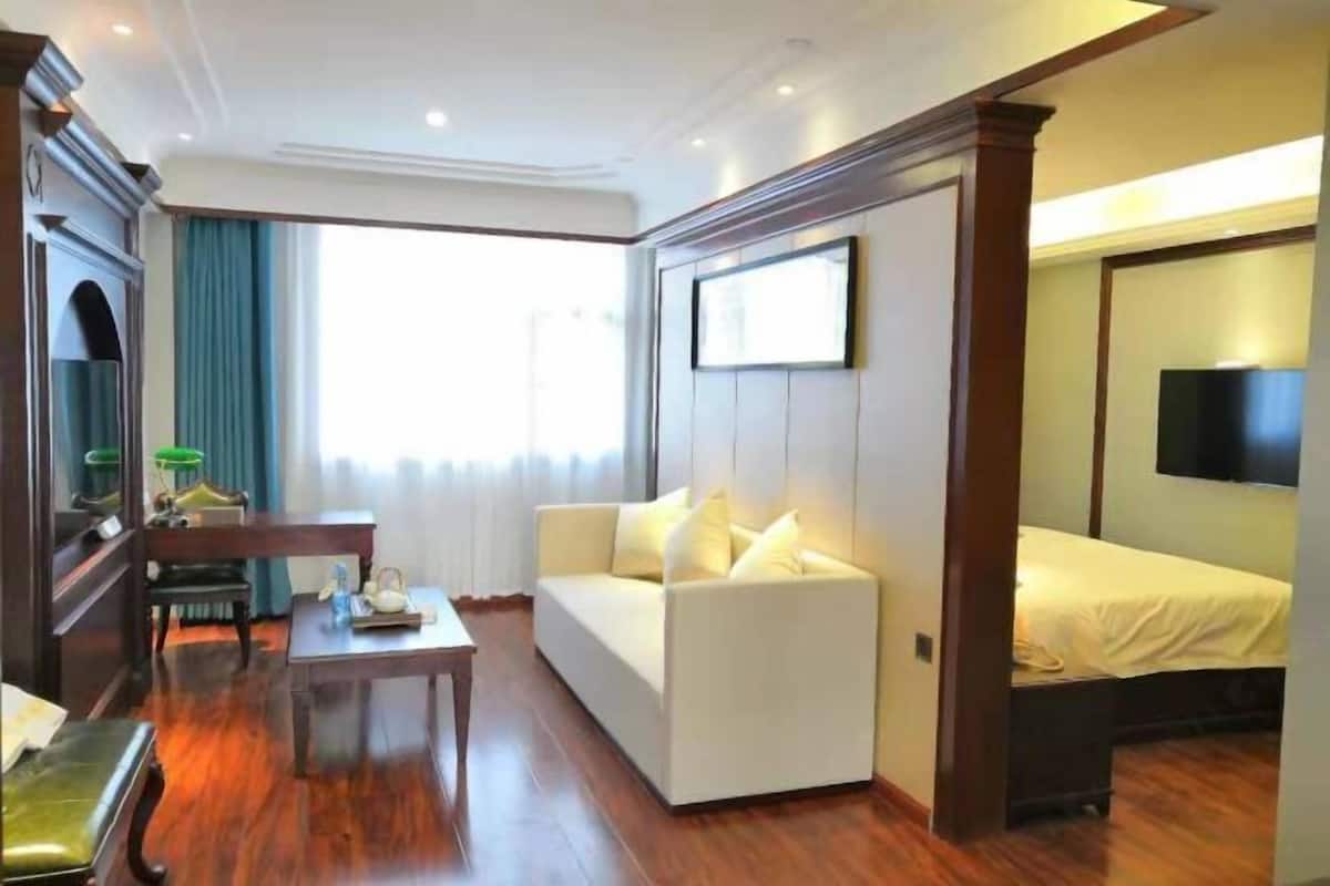 Habitación de hotel con sofá, cama, televisor, mesa y espejo.