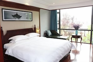 Habitación de hotel con una cama grande, una silla, una mesita y una ventana con vistas a árboles.