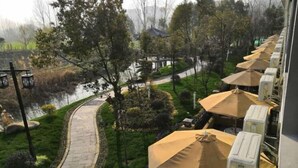 Un chemin menant à un espace extérieur aménagé avec des parasols, entouré de verdure et bordé d’un plan d’eau.