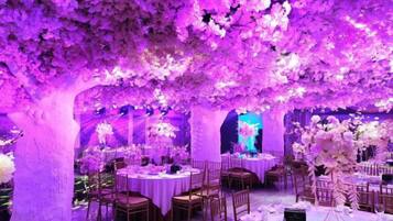 A banquet hall with round tables, chairs, and floral arrangements.