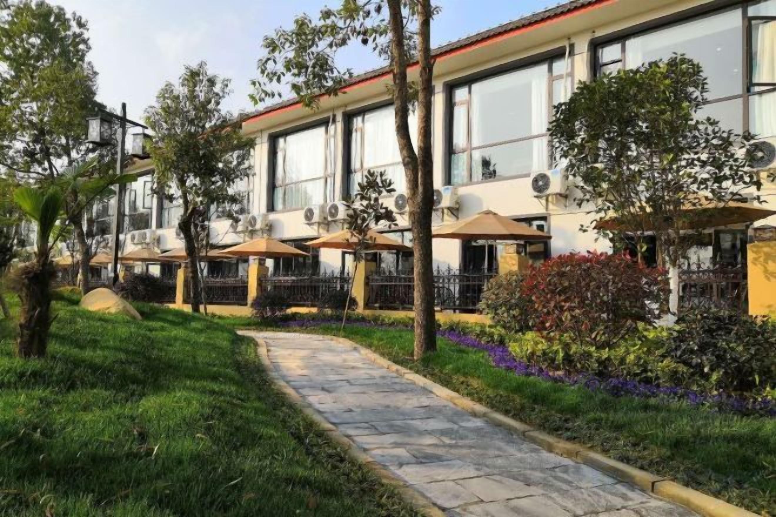 A hotel with outdoor seating, a paved walkway, and a garden with various plants.