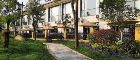 A hotel with outdoor seating, a paved walkway, and a garden with various plants.