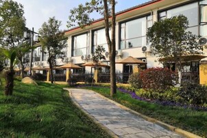 Un hotel con terraza al aire libre, un camino pavimentado y un jardín con diversas plantas.