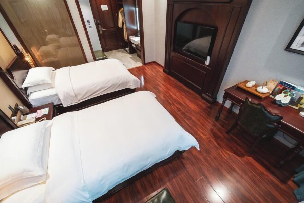 Ein Hotelzimmer mit zwei Betten, Holzboden, Fernseher, einem kleinen Tisch mit Stuhl und einem Kleiderschrank.