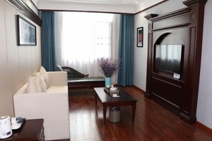 Ein Hotelzimmer mit einer Couch, einem Couchtisch, einem Fernseher und einem Fenster mit Vorhängen.