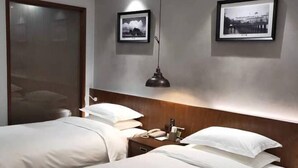 Une chambre d’hôtel avec deux lits, une tête de lit en bois, une table de chevet avec une lampe et deux tableaux encadrés au mur.
