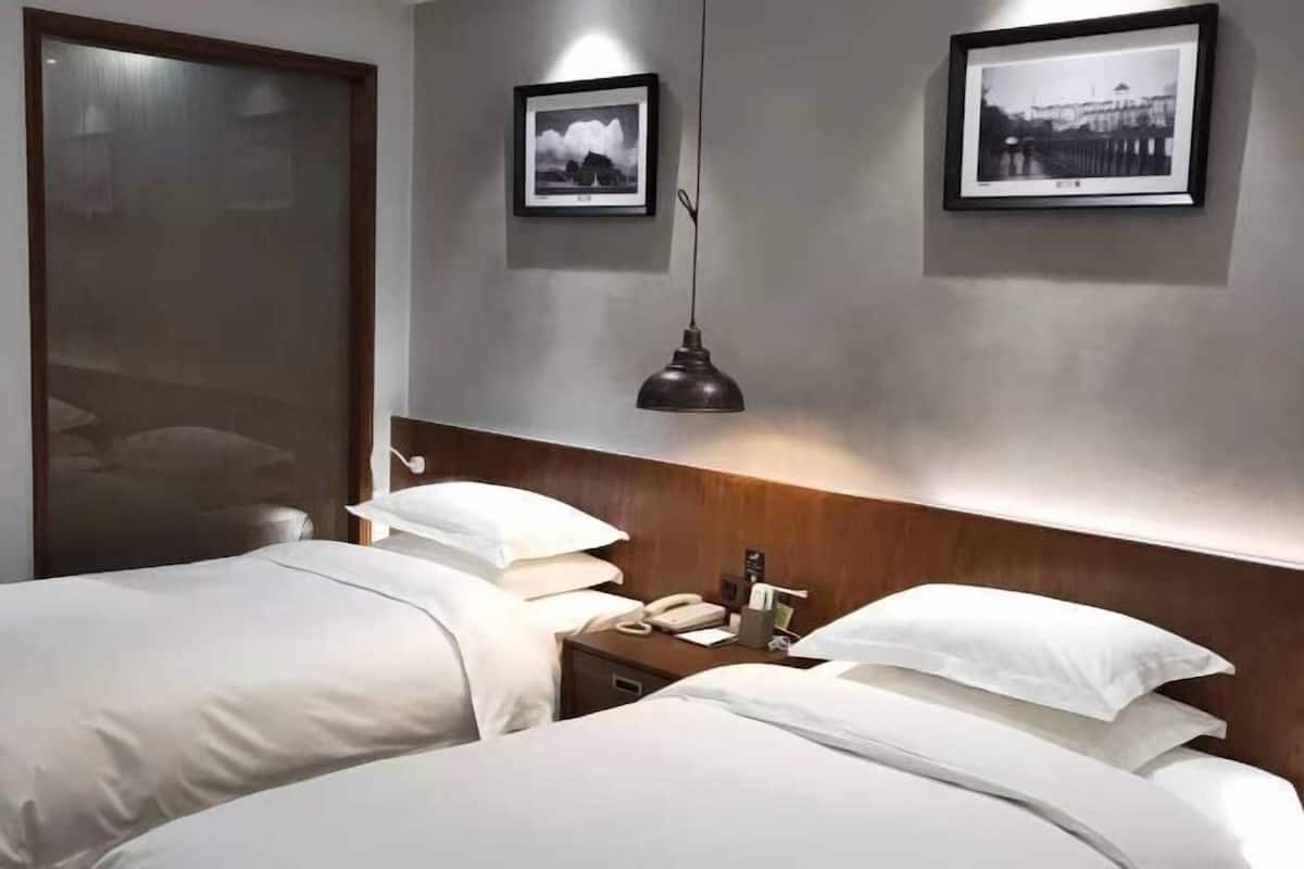 Habitación de hotel con dos camas, un cabecero de madera, una mesita de noche con lámpara y dos cuadros enmarcados en la pared.