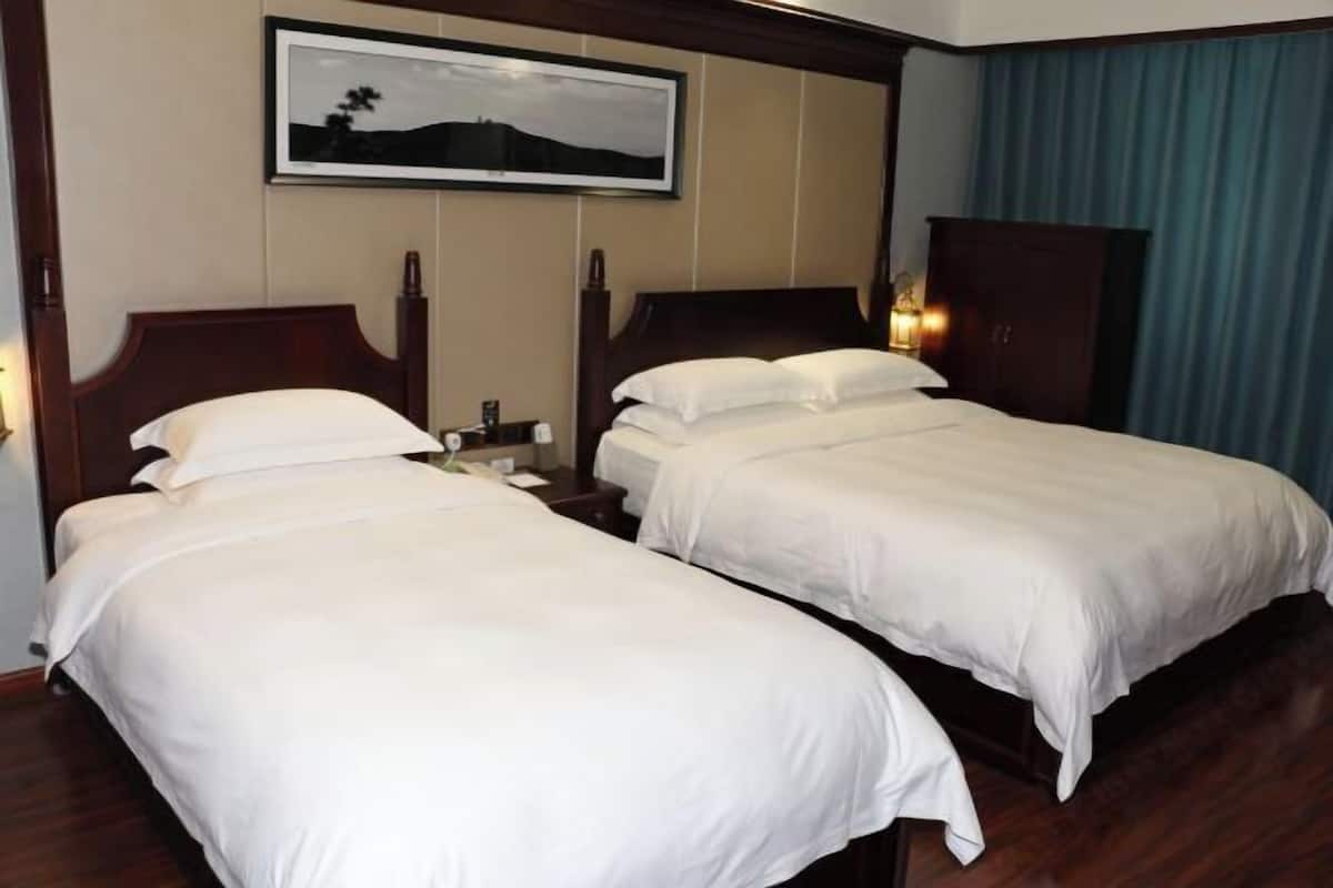 Habitación de hotel con dos camas individuales, cabecera de madera, mesita de noche, lámpara y un cuadro en la pared.