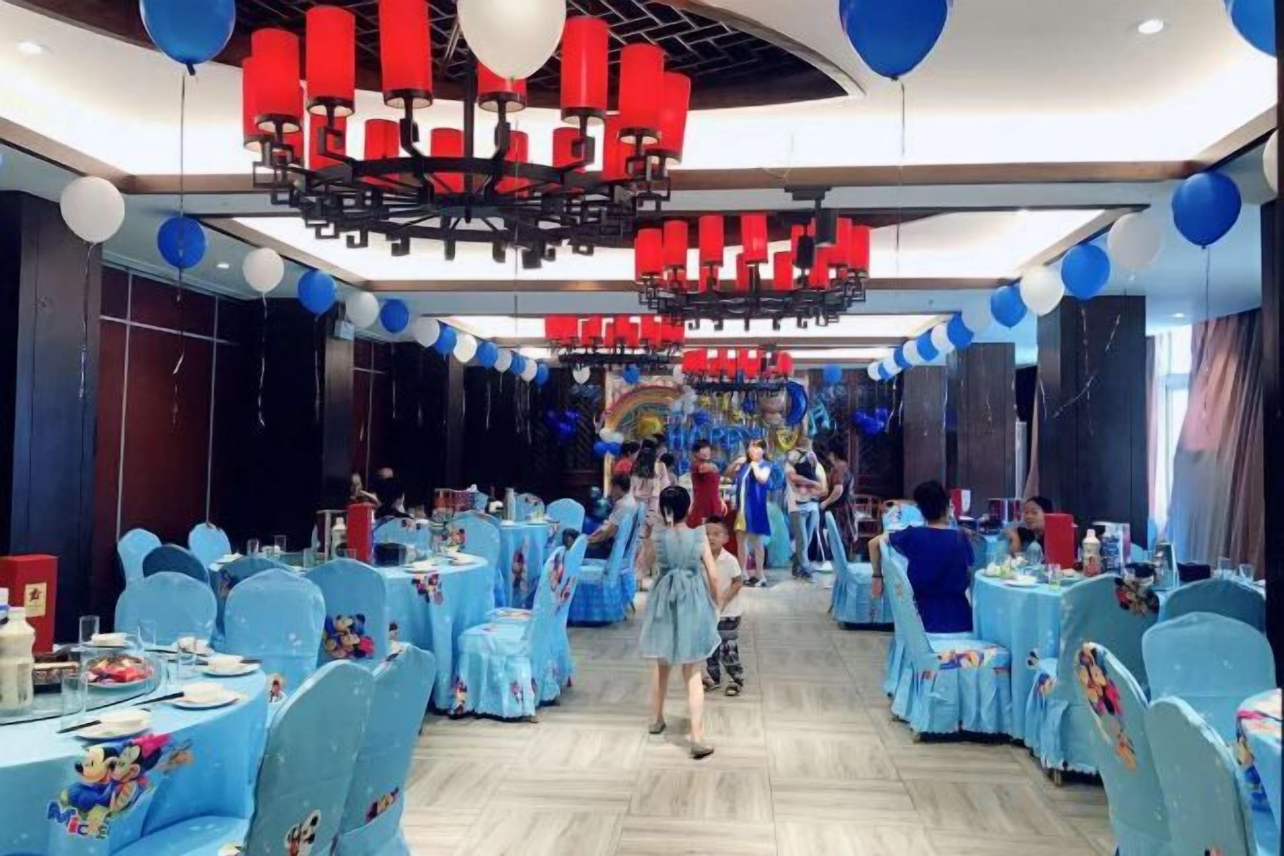 Ein Festsaal mit runden Tischen, blauen Stühlen und roten und weißen Ballons.