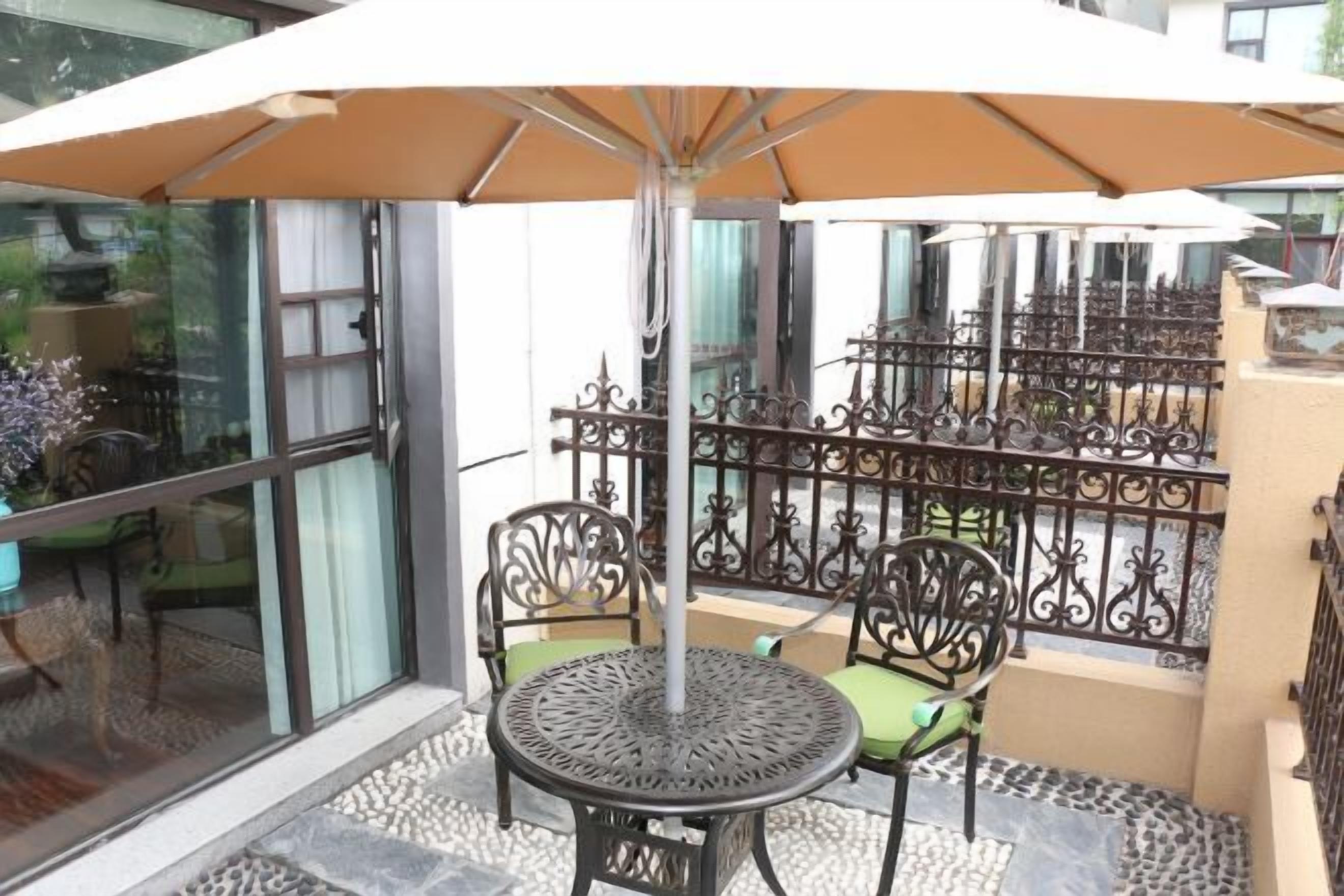 Un área de estar al aire libre techada con una mesa redonda y dos sillas, una sombrilla grande y una valla decorativa de metal.