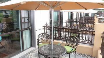 Un área de estar al aire libre techada con una mesa redonda y dos sillas, una sombrilla grande y una valla decorativa de metal.